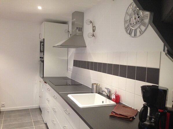 A modern kitchen with a built-in oven, a stainless steel range hood, a white sink, and a black coffee maker.