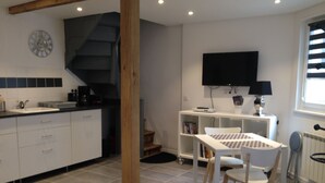 A modern kitchen with white cabinets, a black countertop, and a built-in stove. There is a dining area with a white table and chairs, and a TV mounted on the wall.