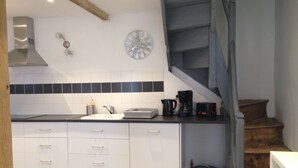 A modern kitchen with white cabinets, a black countertop, a stainless steel range hood, a clock, and a staircase leading to a lower level.