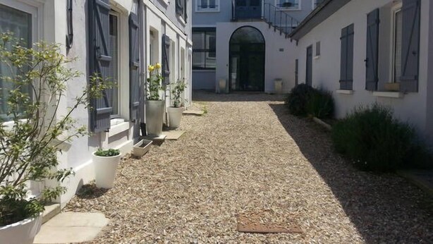 A courtyard with a gravel path, potted plants, and a building with a large arched entrance.