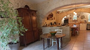 A rustic kitchen with stone walls, a wooden cabinet, a dining table with chairs, and a potted plant. - Large family home with character, south of France + independent studio apartment (Souvignargues)