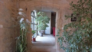 A stone-walled hallway with a staircase leading to a room. There are potted plants on either side of the stairs and a large window with bars. - Large family home with character, south of France + independent studio apartment (Souvignargues)