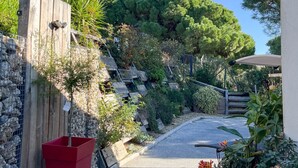 Un sendero pavimentado que conduce a una escalera de madera rodeada de vegetación y un muro de piedra.