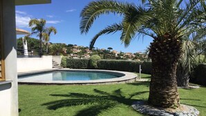 Una piscina rodeada de césped cuidado y palmeras, con vistas a casas al fondo.