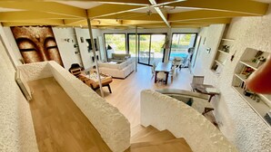 A spacious living area with a wooden floor, a sofa, a coffee table, and a foosball table. There is a large window providing a view of the outdoors.