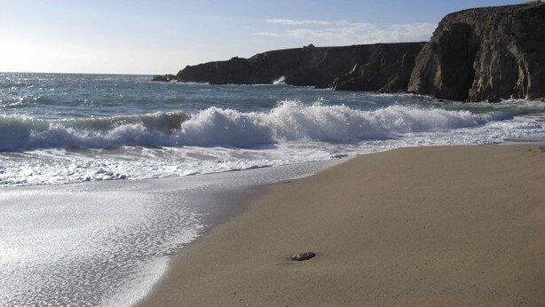 A beach with waves crashing onto the shore, a sandy beach, and rocky cliffs in the background.