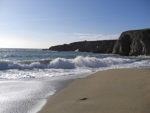 A beach with waves crashing onto the shore, a sandy beach, and rocky cliffs in the background.