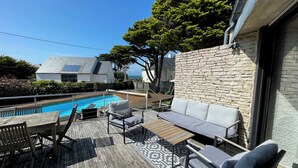 A poolside area with a wooden deck, a stone wall, and a seating area with a sofa and chairs.