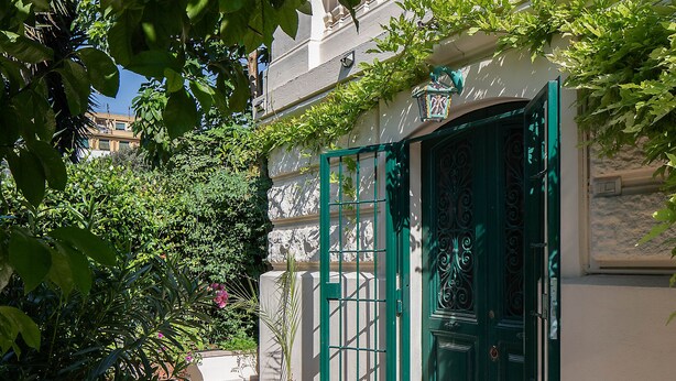 A narrow pathway leading to a building with a green door and a balcony.