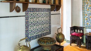 A room with a bookshelf, a decorative wall hanging, a tiled floor, and a traditional tea set.