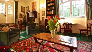 A cozy living room with a wooden coffee table, a bookshelf, and a large window with curtains.