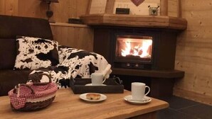 A cozy cabin interior with a wooden interior, a fireplace, a sofa with a cow print blanket, a table with a basket and a plate, and a heart-shaped decoration on the wall.