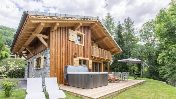 A wooden cabin with a hot tub, deck, and outdoor seating area.
