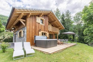 A wooden cabin with a hot tub, deck, and outdoor seating area.