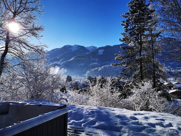 Un paysage enneigé avec des montagnes en arrière-plan et une terrasse en bois au premier plan.