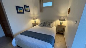 Un dormitorio con una cama, dos mesitas de noche, dos lámparas, un ventanal y dos cuadros colgados en la pared.