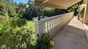 Un espacio al aire libre cubierto con balaustrada blanca, un farol negro, y un jardín con diversas plantas y flores.