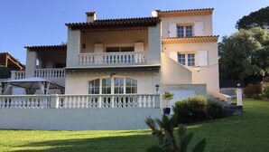 Una casa de dos pisos con balcón, cerca viva blanca y césped cuidado.