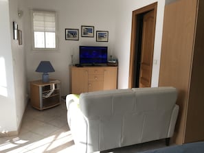 A living room with a sofa, a TV on a wooden cabinet, a lamp, and framed pictures on the wall.