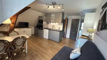 Eine kompakte Küche mit modernen Geräten, ein Essbereich mit Korbstühlen und ein gemütlicher Wohnbereich mit Sofa und Zierkissen.