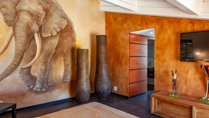 Un interior moderno con un gran mural de elefantes, muebles de madera y un televisor montado en la pared.