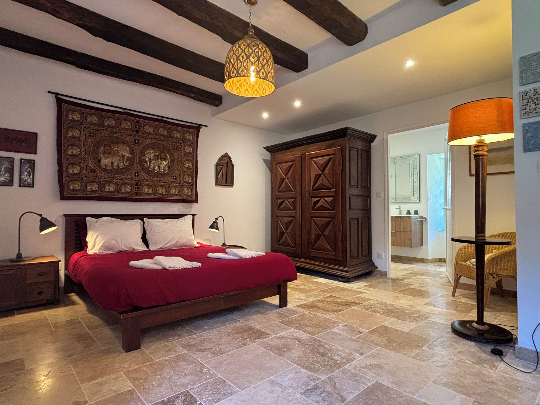 Une chambre avec un grand lit, une armoire en bois, un luminaire suspendu et une lampe sur pied.