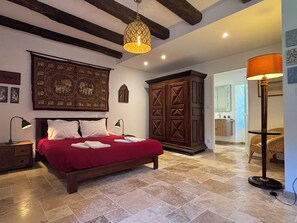 A bedroom with a large bed, a wooden wardrobe, a hanging light fixture, and a floor lamp.