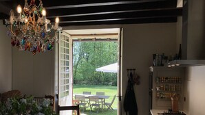 Una puerta abierta que da a un patio con una mesa y sillas, una araña y una zona de cocina con armarios y una estufa.
