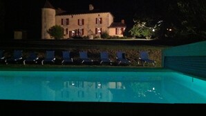 Vista nocturna de un hotel con piscina y sillones de descanso.
