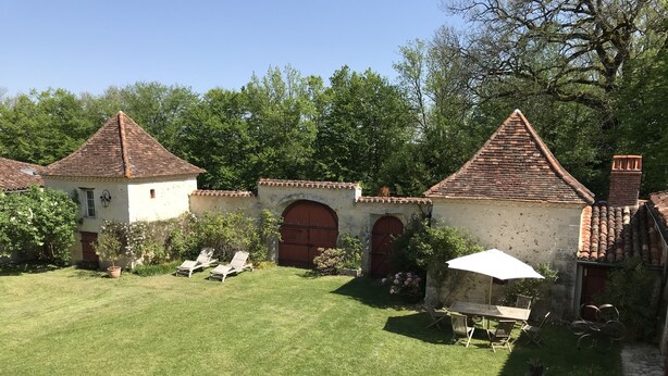 Un patio con césped, dos edificios pequeños con tejados de tejas y una mesa con sombrilla.