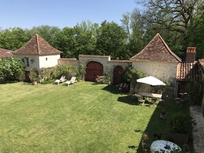 A courtyard with a lawn, two small buildings with tiled roofs, and a table with an umbrella.
