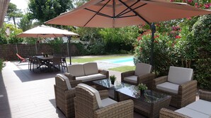A patio area with wicker furniture, a glass table, and two large umbrellas providing shade. - Villa 600 m from the beach, heated swimming pool 9x4, classified 3*. (Labenne)