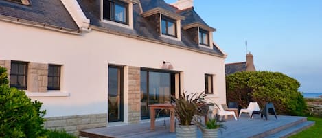 A modern house with a sloped roof, large windows, and a covered patio area with outdoor furniture.
