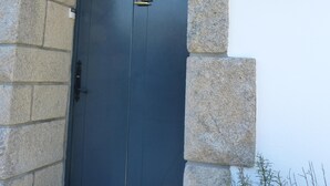 Eine dunkelblaue Tür mit einem kleinen dreieckigen Fenster und einer goldfarbenen Klinke, eingebettet in einen steinernen Bogen.