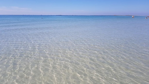 Ein sauberer Strand mit ruhigem Wasser und einer fernen Küstenlinie.