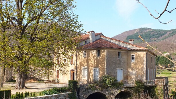 Ein Haus aus Stein mit rotem Ziegeldach, einer Steinsäule und einer kleinen Brücke.