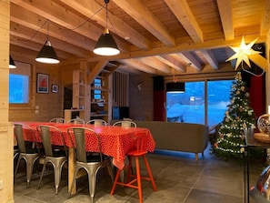 Comedor con techo de madera, un árbol de Navidad y vista a un paisaje nevado.