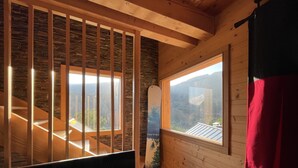 Un intérieur en bois avec un escalier menant à un balcon, un mur en pierre et une fenêtre donnant sur la montagne.
