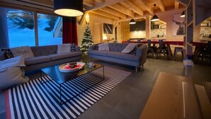 Un salon chaleureux avec un canapé et une table basse, un sapin de Noël et une cuisine en arrière-plan.