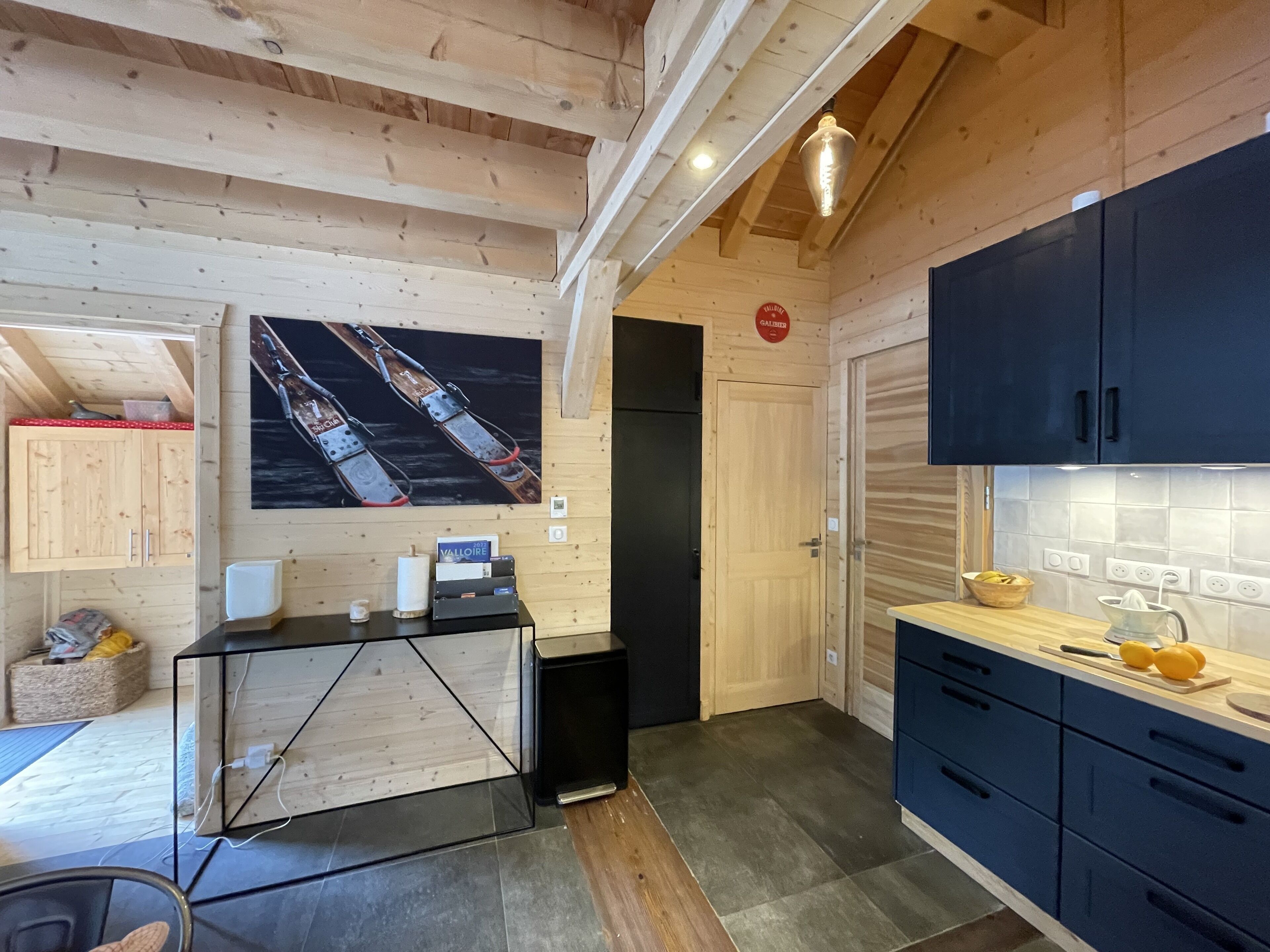 Un interior de madera con una zona de cocina que cuenta con gabinetes azul oscuro, salpicadero de azulejos y techo de madera con vigas a la vista.