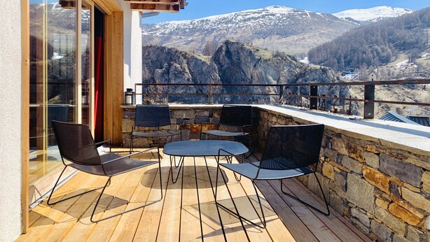 Un balcon doté d’un plancher en bois, de murs en pierre et de chaises en métal noir.