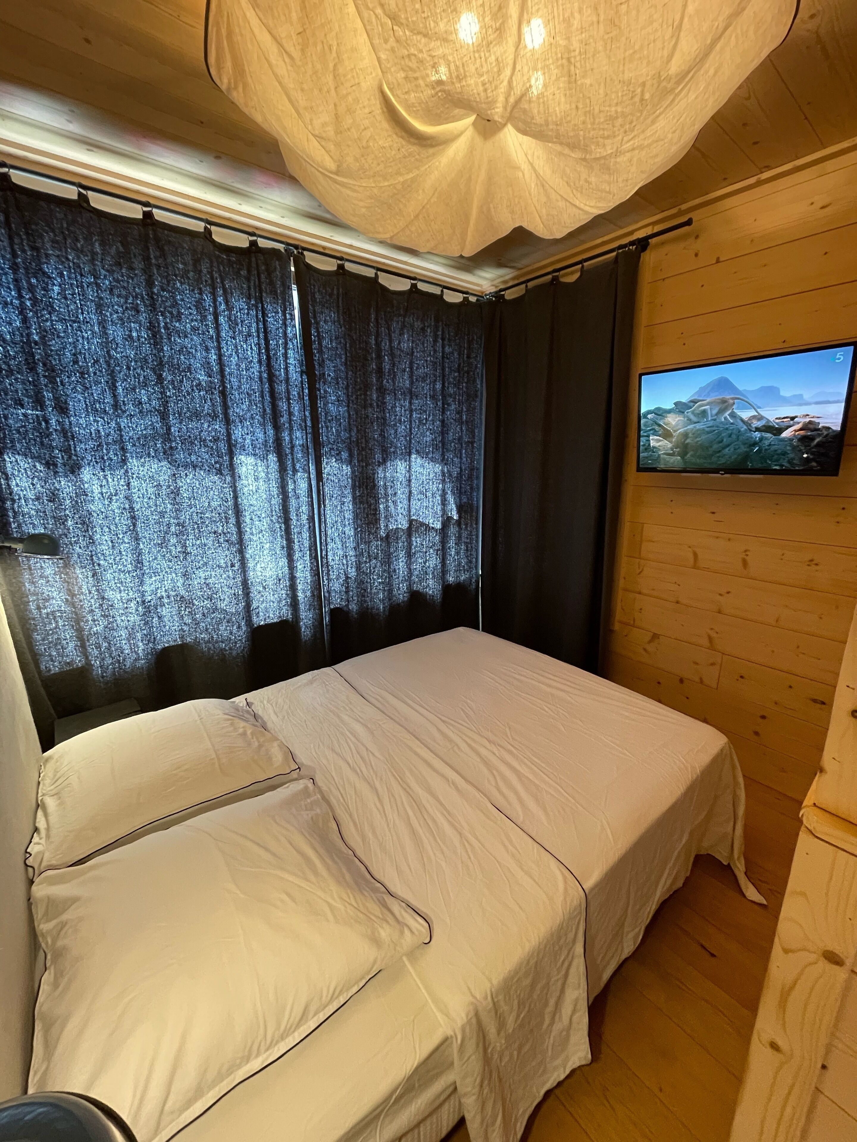 Un dormitorio con cama, cortinas, un televisor en la pared y paneles de madera.