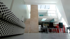 Un'ampia hall con soffitto alto, un divano a scacchi, una scala e vista sul cielo tramite finestre a lucernario.