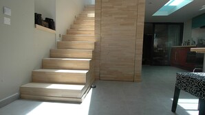 Una scala con gradini in legno conduce a un pianerottolo, un angolo cottura con mobili ed elettrodomestici, e un tavolo con decorazioni.