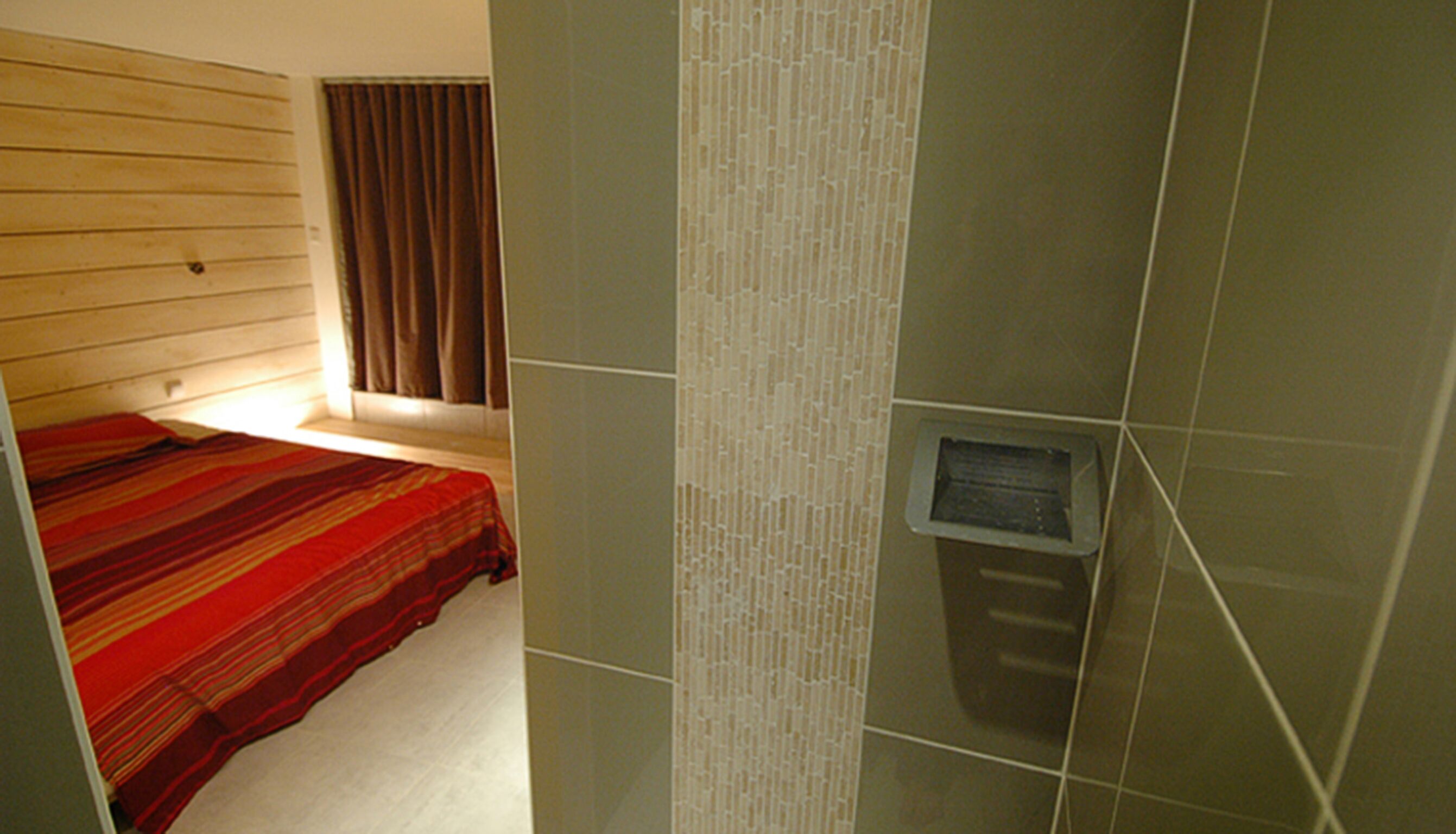 A room with a bed, a window with curtains, and a wall-mounted heater.