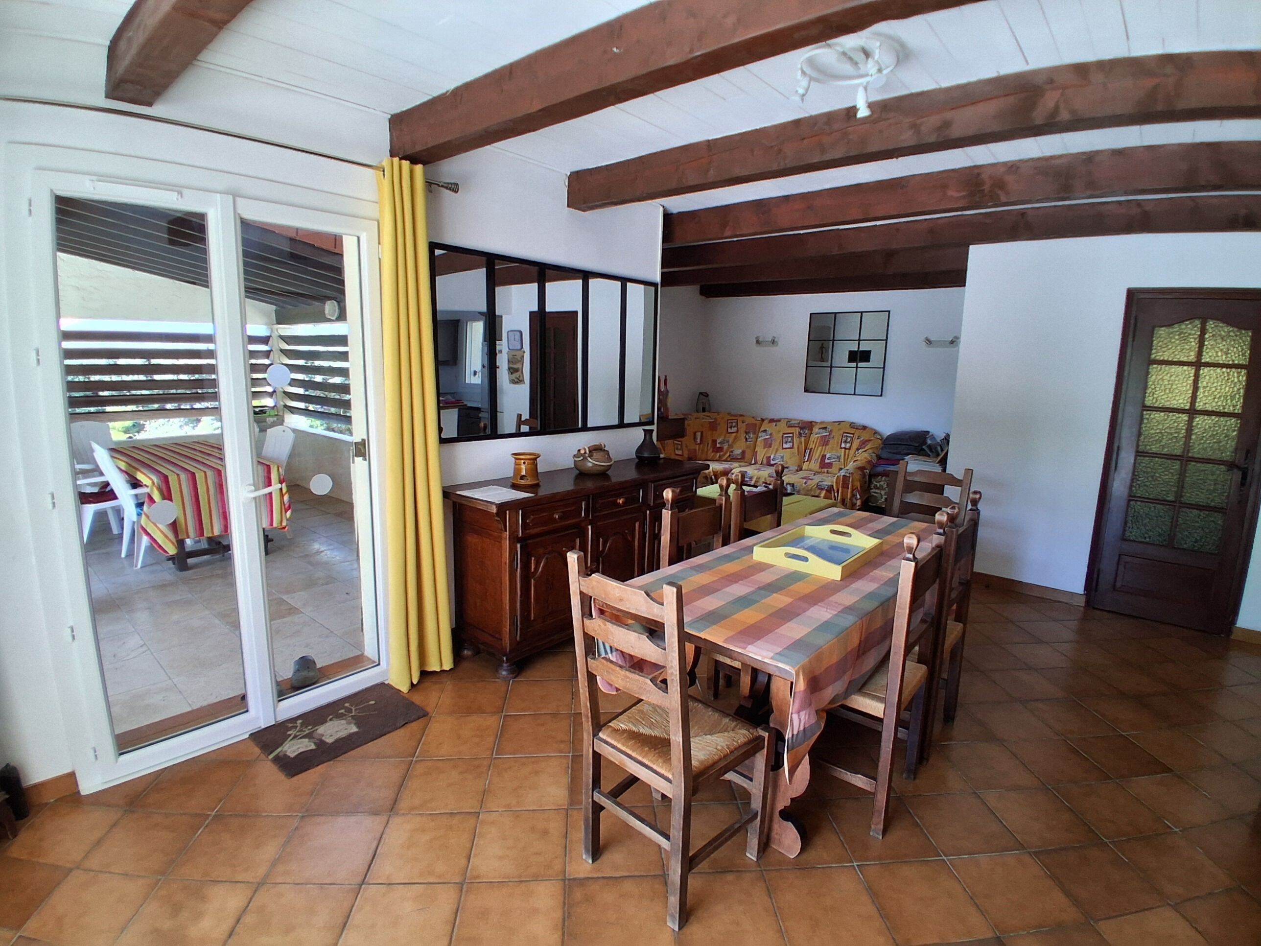 Un espace repas avec une table et des chaises en bois, un coin cuisine avec un comptoir et des placards, et une porte-fenêtre coulissante donnant sur un patio extérieur.