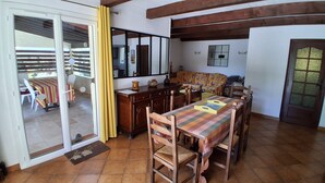 Un comedor con mesa y sillas de madera, una zona de cocina con encimera y armarios, y un ventanal corredizo que da a un patio exterior.