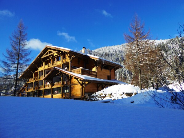 Un chalet en bois doté d’un balcon, entouré d’arbres couverts de neige et avec une montagne en arrière-plan.