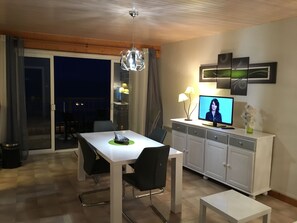 A modern dining area with a white table and chairs, a TV on a cabinet, and a balcony with a view. - SPACIOUS APARTMENT WITH LARGE BALCONY FACING THE SEA (Saint-Jean-De-Monts)