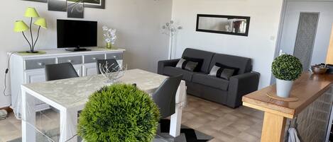 A modern living room with a dining area, a gray sofa, a TV, and decorative wall art.